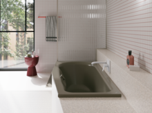 Olivgrüne Badewanne in hellem Bad mit weißen Fliesen, Fenster, rotem Hocker und Armatur.