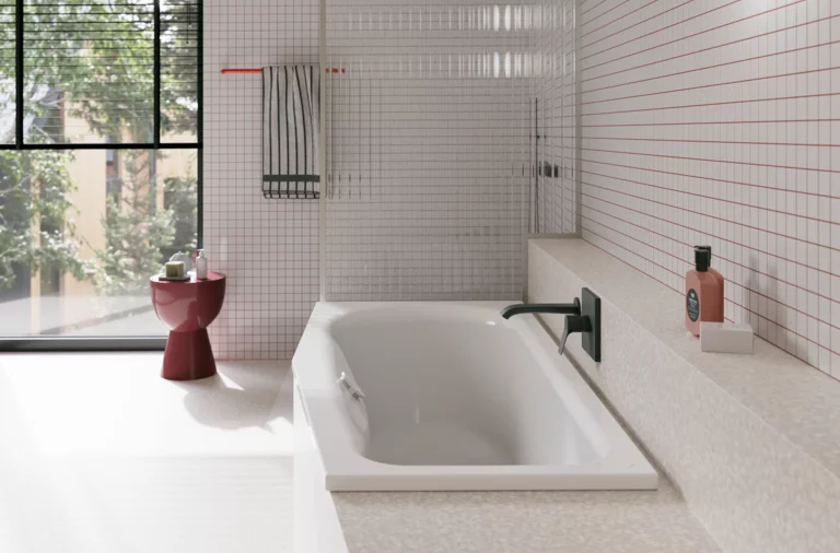 Weiße Badewanne in hellem Bad mit weißen Fliesen, großem Fenster, schwarzer Armatur und rotem Hocker.
