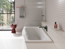 Weiße Badewanne in hellem Bad mit weißen Fliesen, großem Fenster, schwarzer Armatur und rotem Hocker.