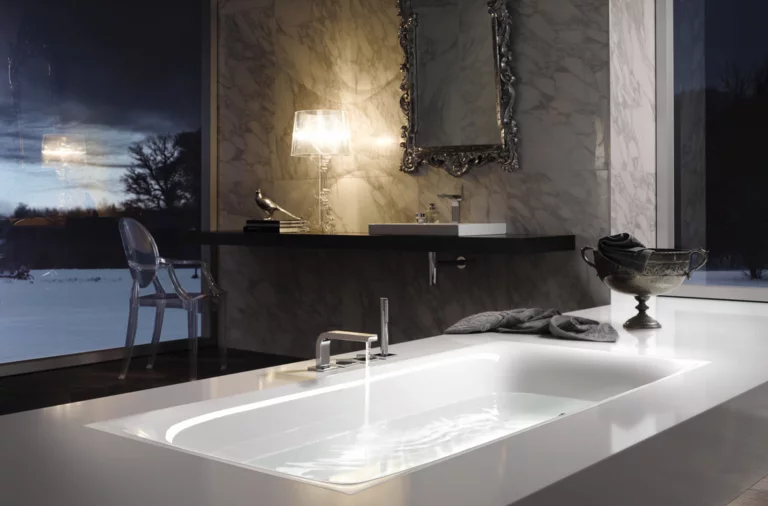 Baignoire rectangulaire en acier émaillé, lavabo rectangulaire sur plan noir, salle de bain luxueuse avec mur en marbre.