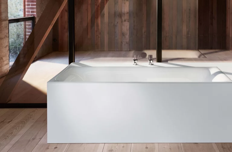Rechteckige Badewanne aus Stahl-Email, weiß, freistehend in modernem Raum mit Holz- und Glaselementen.