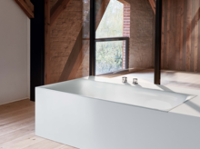 Baignoire rectangulaire en acier émaillé, autoportante, aux lignes épurées dans une pièce lumineuse et moderne avec des éléments en bois.
