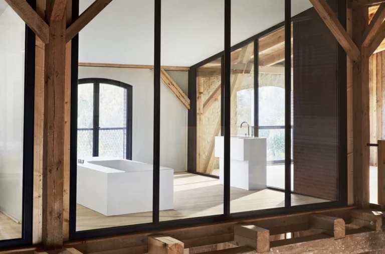 Vue à travers la façade vitrée sur une salle de bains avec baignoire encastrée rectangulaire et lavabo en bois rustique.