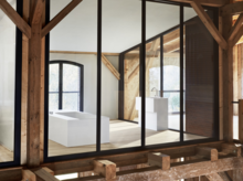 Vue à travers la façade vitrée sur une salle de bains avec baignoire encastrée rectangulaire et lavabo en bois rustique.