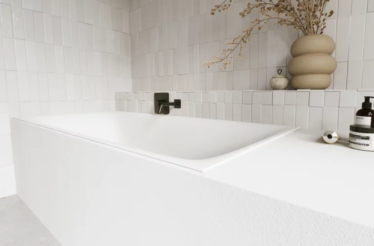 Weiße Badewanne in hellem Bad mit weißen Fliesen, schwarzer Armatur, Vase und Pflegeprodukten.