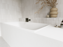 Weiße Badewanne in hellem Bad mit weißen Fliesen, schwarzer Armatur, Vase und Pflegeprodukten.