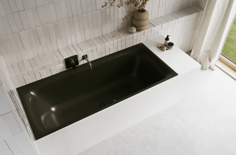 Schwarze Badewanne in hellem Bad mit weißen Fliesen, schwarzer Armatur, Vase mit Zweigen und Vorhang.