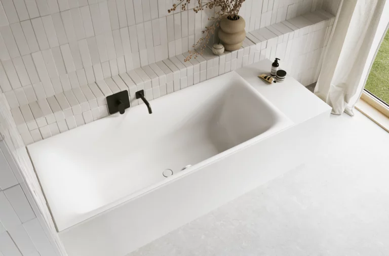 Weiße Badewanne in hellem Bad mit weißen Fliesen, schwarzer Armatur, Vase mit Zweigen und Vorhang.