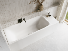 Weiße Badewanne in hellem Bad mit weißen Fliesen, schwarzer Armatur, Vase mit Zweigen und Vorhang.