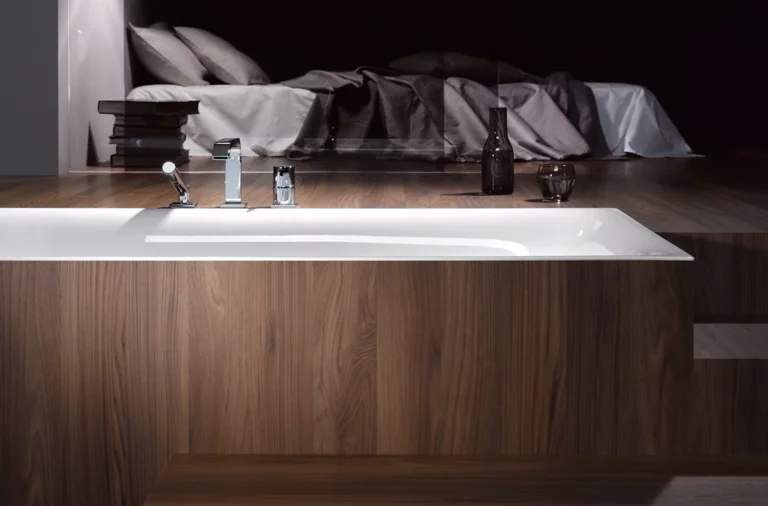 Baignoire rectangulaire en acier émaillé avec habillage bois, design moderne, marches au premier plan, chambre à coucher en arrière-plan.