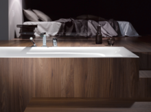 Baignoire rectangulaire en acier émaillé avec habillage bois, design moderne, marches au premier plan, chambre à coucher en arrière-plan.