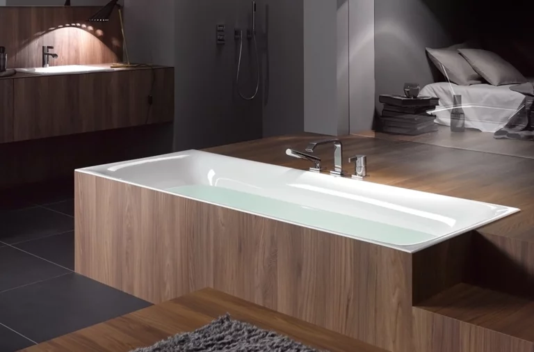 Rechteckige Stahl-Email-Badewanne, halb eingelassen in Holzverkleidung, daneben Waschbecken auf Einbauplatte und moderne Badezimmerausstattung.