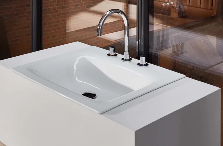 Стальная эмалированная раковина прямоугольной формы на белой встраиваемой панели с трехрычажным смесителем.