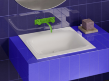 Weißes Waschbecken auf violett gefliestem Waschtisch, mit grüner Wandarmatur vor dunkelblauer Fliesenwand.