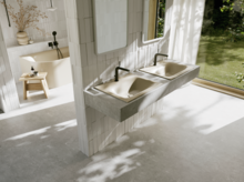 Helles Badezimmer mit zwei beigen Waschtischen, schwarzen Armaturen, großer Fensterfront und Blick in den grünen Garten.