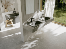 Helles Badezimmer mit zwei dunkelgrauen Waschtischen, schwarzen Armaturen, großer Fensterfront und Blick in den grünen Garten.