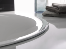 Rundes Waschbecken aus Stahl-Email auf glänzender Einbauplatte, daneben gefaltete Handtücher und eine Glasflasche.