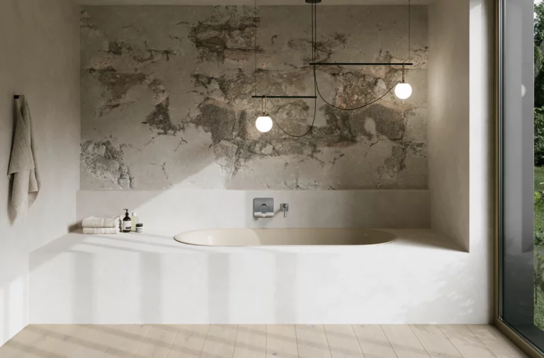 Cremefarbene Badewanne in hellem Bad mit Natursteinwand, Armatur, Pendelleuchten und großem Fenster.