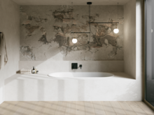 Weiße Badewanne in hellem Bad mit Steinoptik-Wand, schwarzer Armatur, Pendelleuchten und großem Fenster.