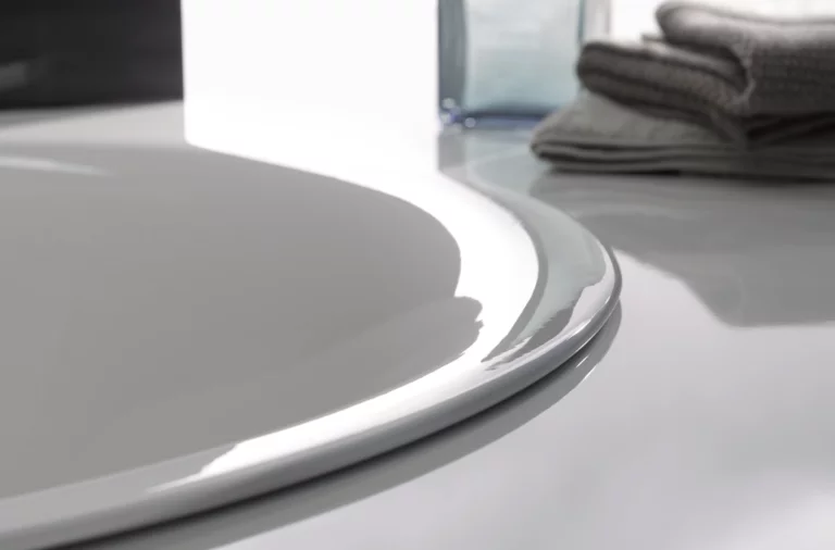 Rundes Waschbecken aus Stahl-Email auf Einbauplatte, glänzende Oberfläche, daneben gefaltete Handtücher und Flasche.