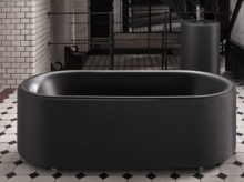 Vrijstaand, ovaal bad van staal-email in zwart, op een betegelde vloer met patroon in een moderne badkamer.