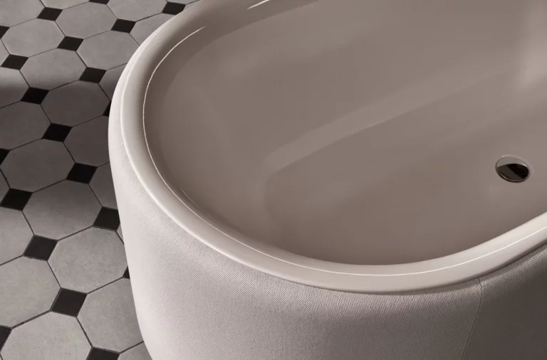 Oval geformte Badewanne aus Stahl-Email auf gemustertem Fliesenboden.