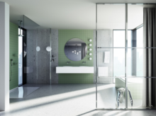 Modern bathroom with green tiles, large glass shower screen, double washbasin, round mirror, and built-in bathtub.