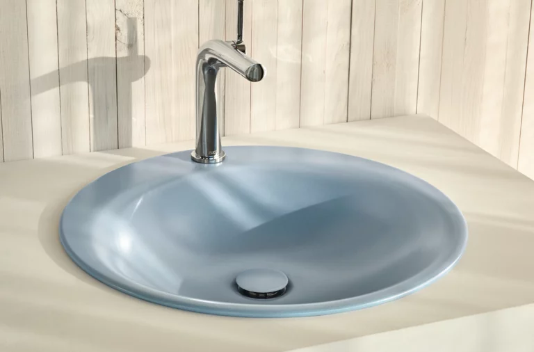Ovales Waschbecken aus Stahl-Email in Einbauplatte mit glänzender Armatur vor heller Holzverkleidung.