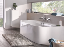 Bañera exenta asimétrica de acero vitrificado en baño moderno con gran ventana y suelo efecto madera.