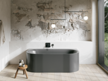 Graue Badewanne in hellem Bad mit Steinoptik-Wand, schwarzer Armatur, Pendelleuchten und großem Fenster.