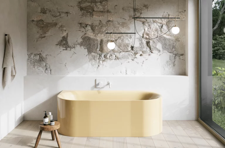 Hellgelbe Badewanne in hellem Bad mit Steinoptik-Wand, Armatur, Pendelleuchten und großem Fenster.
