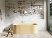 Hellgelbe Badewanne in hellem Bad mit Steinoptik-Wand, Armatur, Pendelleuchten und großem Fenster.