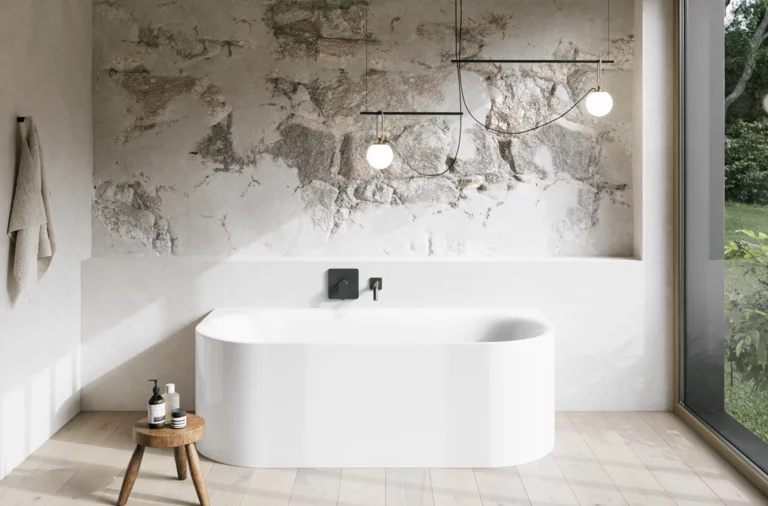 Weiße Badewanne in hellem Bad mit Steinoptik-Wand, schwarzer Armatur, Pendelleuchten und großem Fenster.