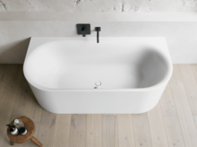 Weiße freistehende Badewanne vor heller Wand mit schwarzer Armatur und Holzfußboden.