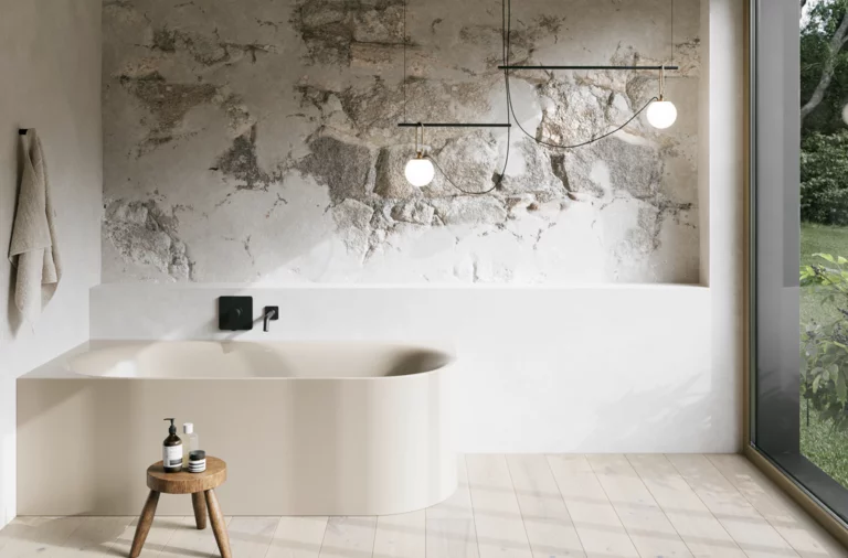 Cremefarbene Badewanne in hellem Bad mit Steinoptik-Wand, schwarzer Armatur, Pendelleuchten und großem Fenster.