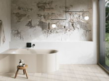 Cremefarbene Badewanne in hellem Bad mit Steinoptik-Wand, schwarzer Armatur, Pendelleuchten und großem Fenster.