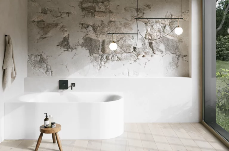 Weiße Badewanne in hellem Bad mit Steinoptik-Wand, schwarzer Armatur, Pendelleuchten und großem Fenster.