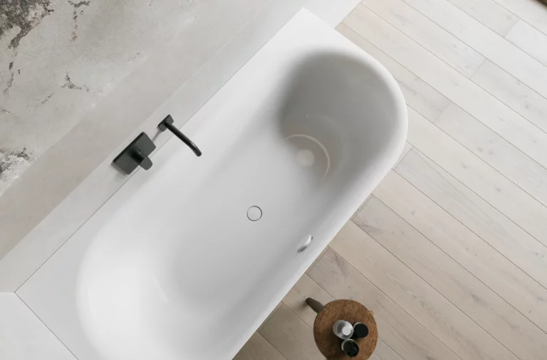 Weiße Badewanne aus der Draufsicht mit schwarzer Armatur, hellem Holzfußboden und kleinem Hocker.