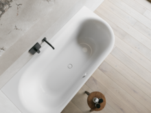 Weiße Badewanne aus der Draufsicht mit schwarzer Armatur, hellem Holzfußboden und kleinem Hocker.