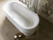 Weiße freistehende Badewanne mit silberner Armatur, hellem Holzfußboden und Steinoptik-Wand.