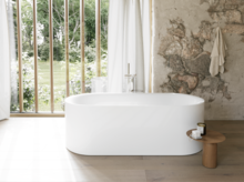Weiße freistehende Badewanne in hellem Bad mit großem Fenster, Steinoptik-Wand und Hocker.
