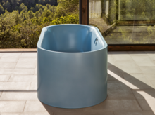 浅蓝色钢瓷独立椭圆浴缸，置于浅色瓷砖上，窗外绿景