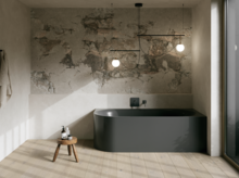 Minimalistisches Bad mit dunkler freistehender Badewanne, Natursteinwand, Hocker und großen Fenstern.