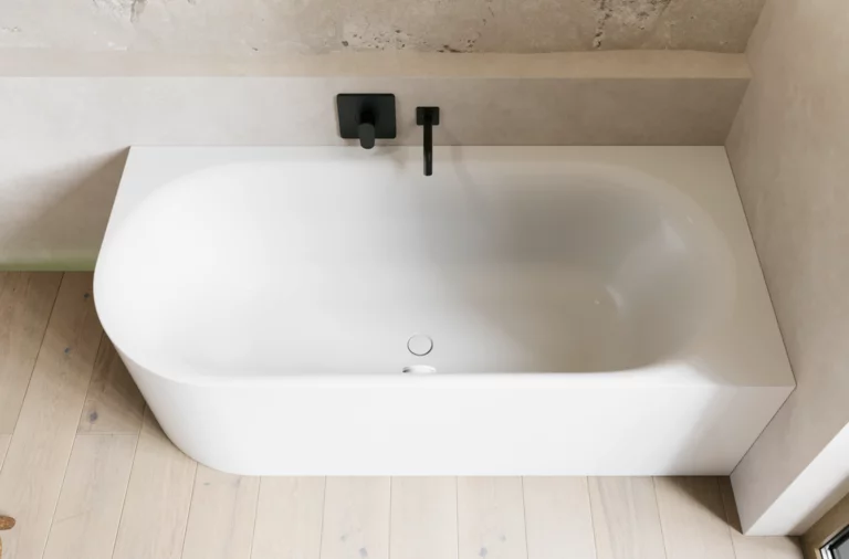 Helles Bad mit weißer Badewanne, schwarzer Wandarmatur, schmaler Ablage und hellem Holzboden.
