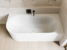 Helles Bad mit weißer Badewanne, schwarzer Wandarmatur, schmaler Ablage und hellem Holzboden.