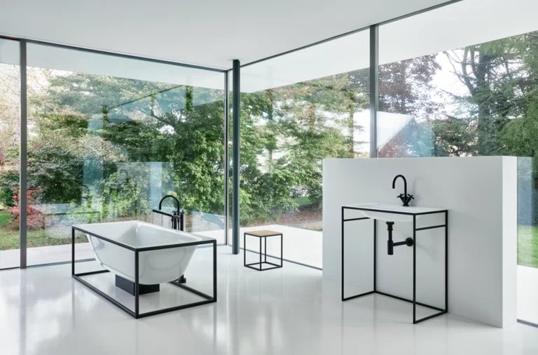 Freestanding rectangular steel enamel bathtub and rectangular washbasin on countertop, modern bathroom with glass front.