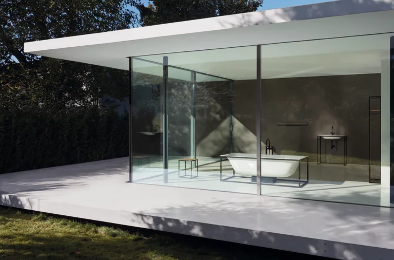 Freestanding rectangular steel-enamel bathtub next to washbasin on countertop in modern glass-walled bathroom.