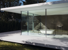 Freestanding rectangular steel-enamel bathtub next to washbasin on countertop in modern glass-walled bathroom.