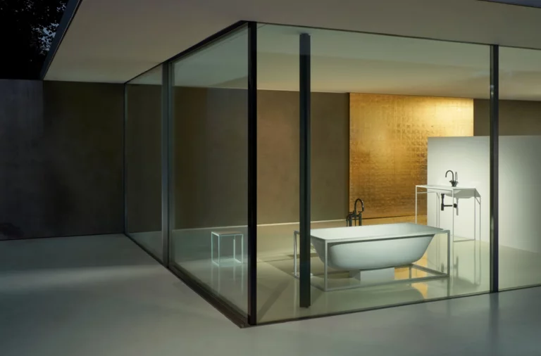 Freestanding, oval steel-enamel bathtub and rectangular washbasin on countertop in modern glass-walled bathroom.