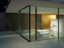 Freestanding, oval steel-enamel bathtub and rectangular washbasin on countertop in modern glass-walled bathroom.